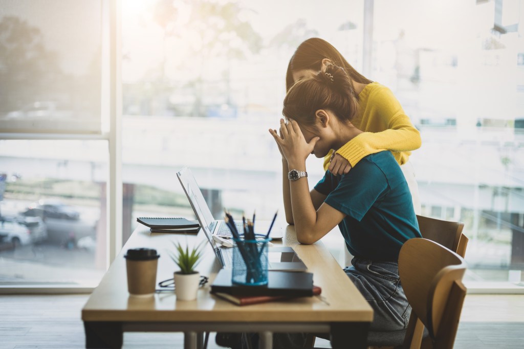 Coworker comforting a stressed and discouraged woman in an office environment